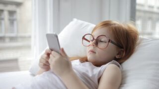 寝ころがってスマホを見るメガネをかけた女の子の写真