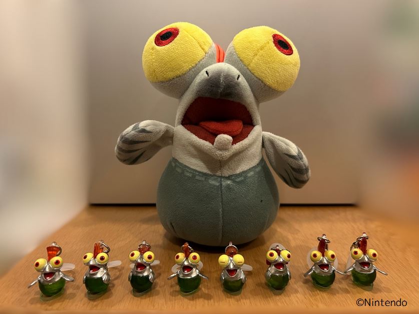 コジャケぬいぐるみの前にコジャケめじるしアクセサリーが８こ並んだ写真。写真右下に©Nintendo