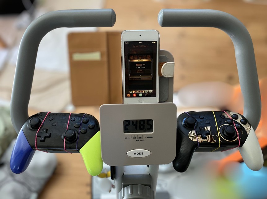 フィットネスバイクのハンドルにコントローラーを2台輪ゴムで取り付けた写真(タブレットトレーにiPodTouchを置いている)