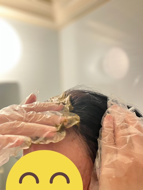 手袋をした手でヘナペーストを前髪に直接塗布している時の写真。